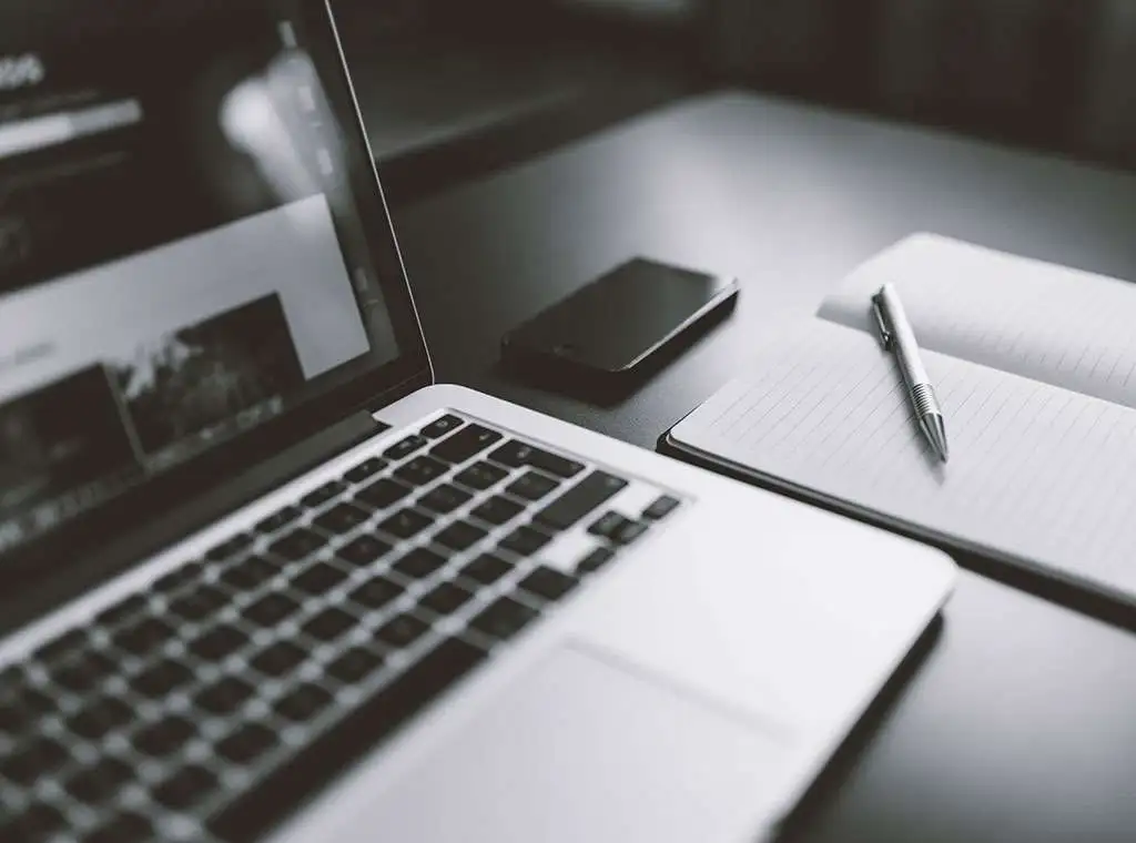 Notebook, phone, pen and paper on a desk in black and white